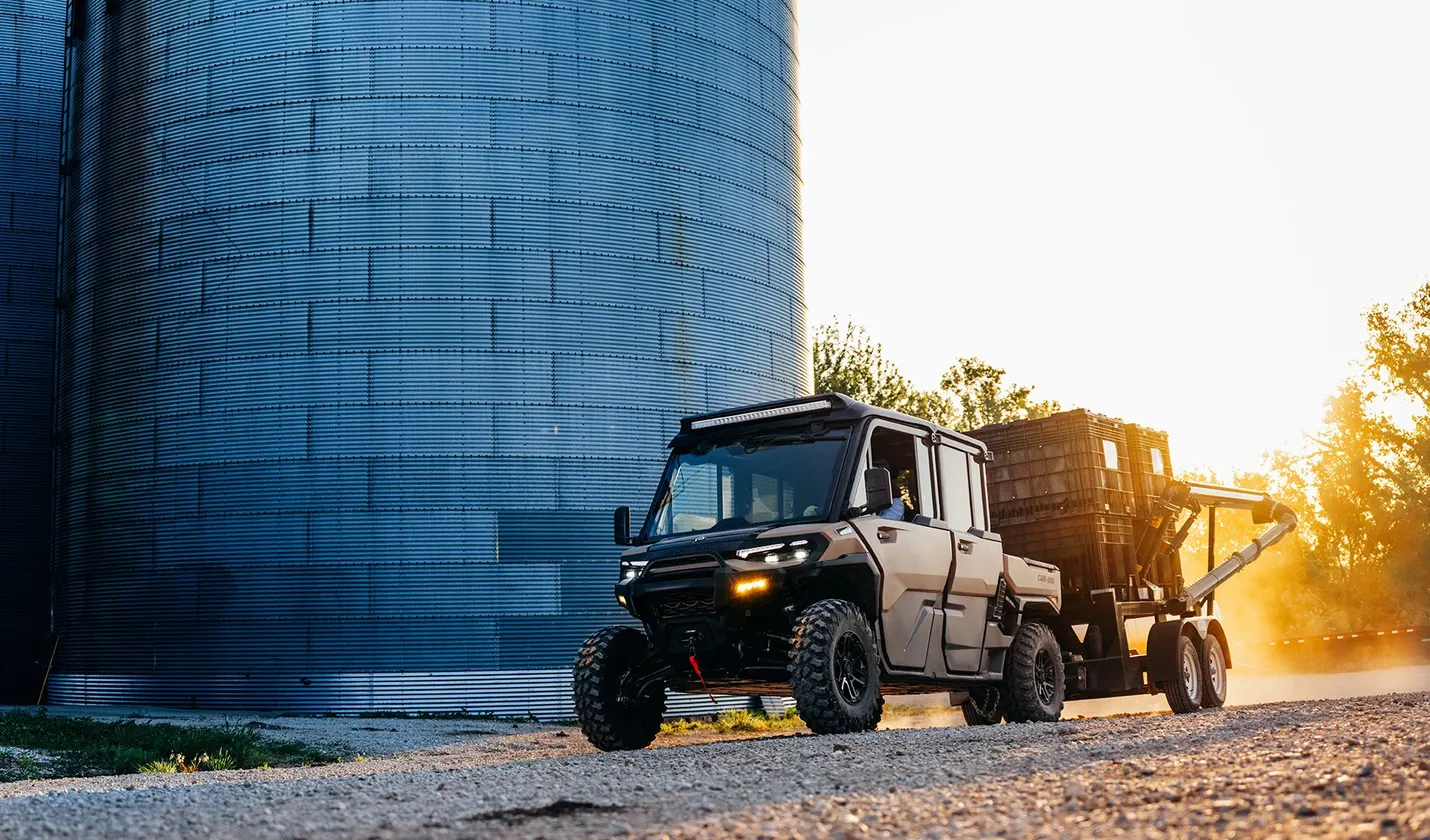 Can-Am Defender MAX pulling a grain cart past a silo