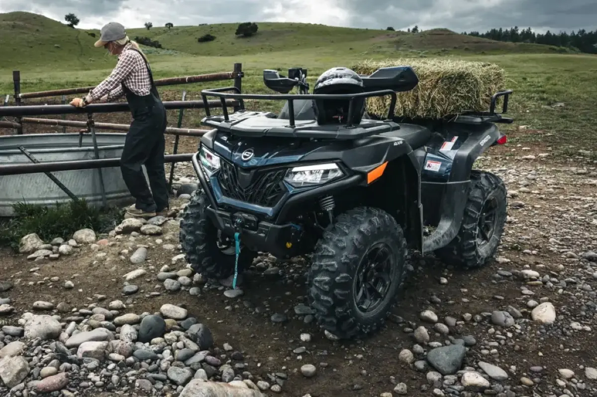 CFMOTO CFORCE utility ATV loaded with hay beside a wooden fence, a rancher working behind it