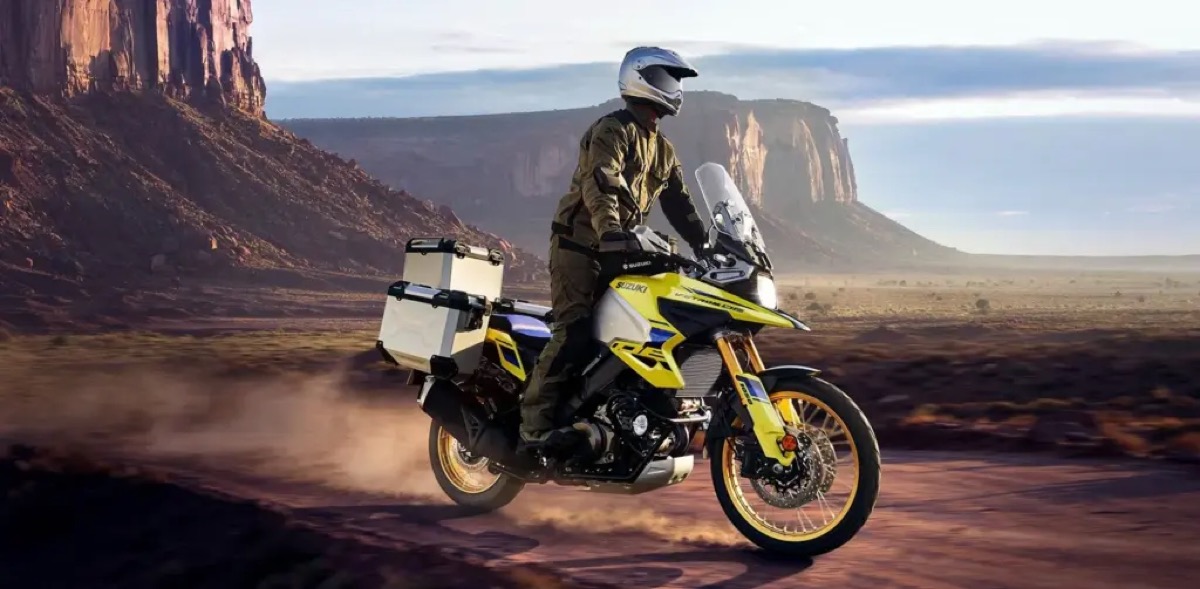 Rider on a yellow Suzuki V-Strom adventure bike on a desert road with mesas behind